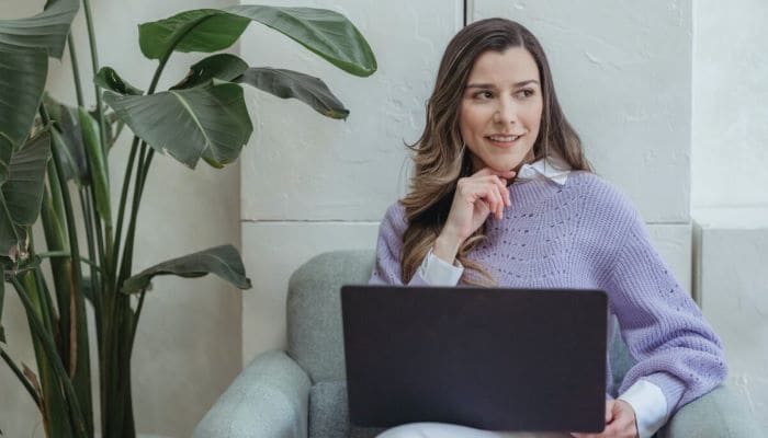Mujer sentada en un sillón con su laptop en las piernas redactando los objetivos SMART de su empresa.