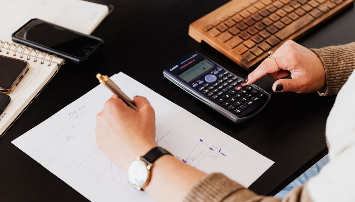 Pessoa fazendo cálculos com calculadora científica e papel e caneta, como se fosse um servidor do ramo da contabilidade pública
