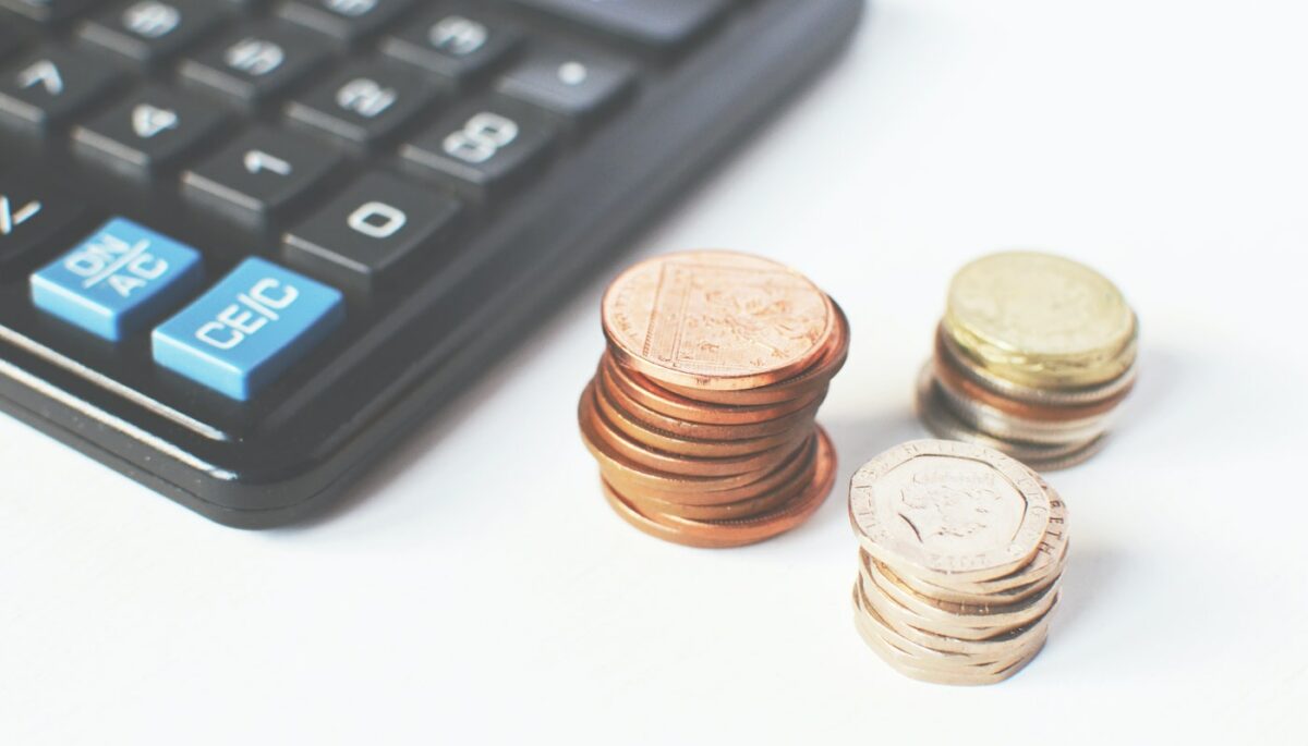 Torres de moedas posicionadas ao lado de calculadora, como se fosse de um lojista cogitando começar com a precificaçao dinamica