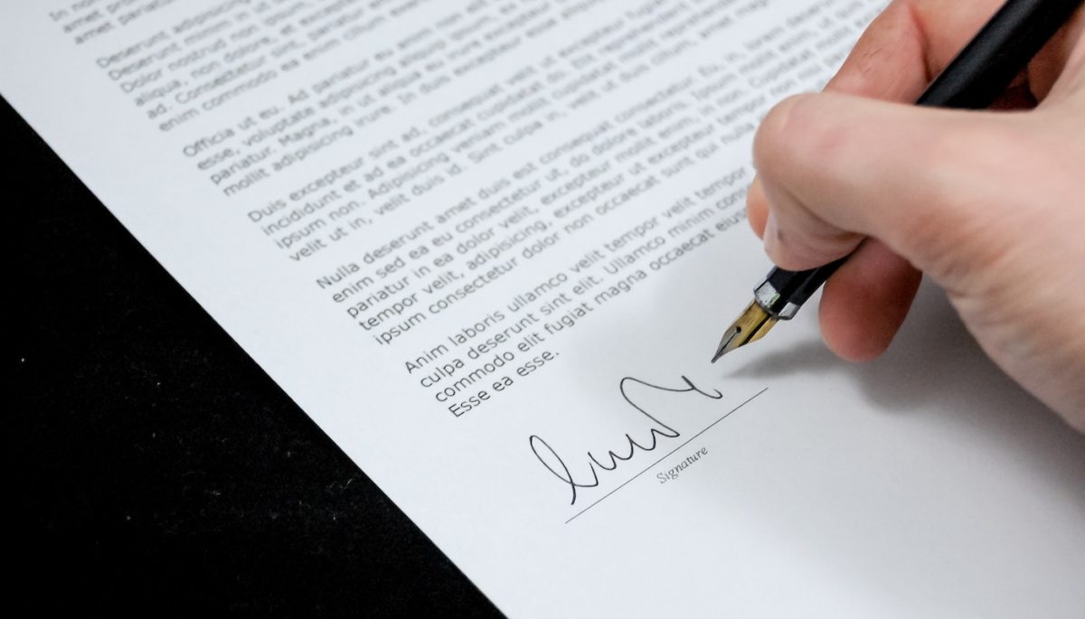 Na imagem, vemos uma carta sendo assinada por uma pessoa.