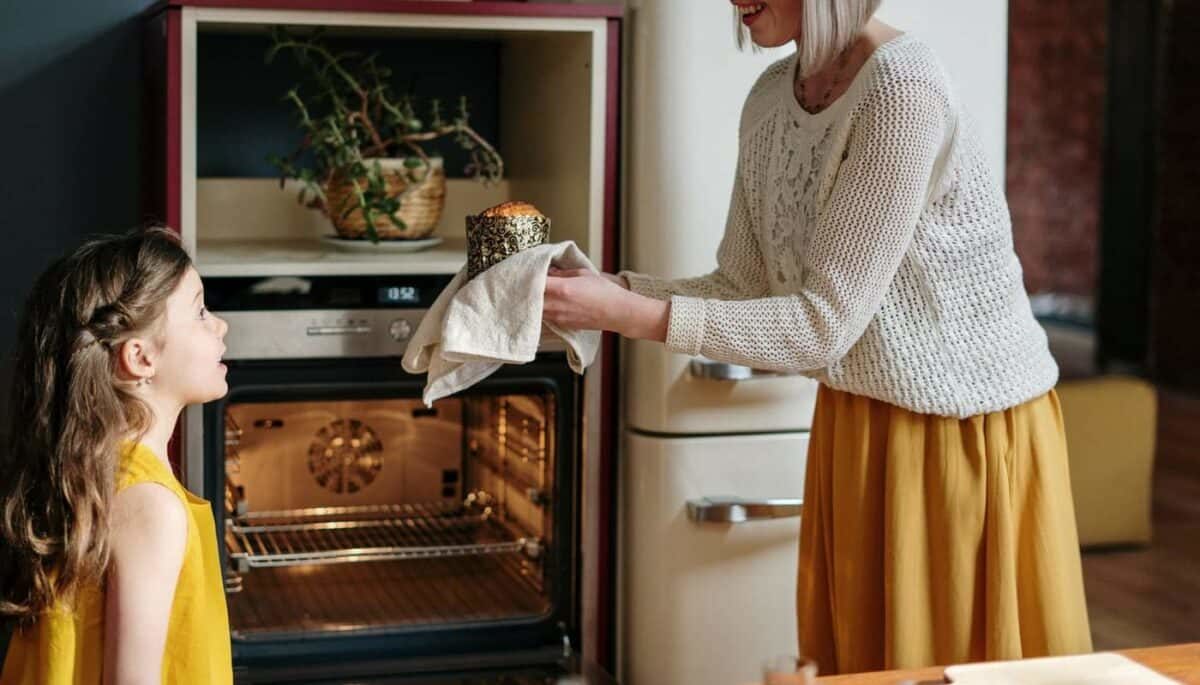 Mulher utilizando um pano de prato para segurar um bolo e entregar para uma menina.