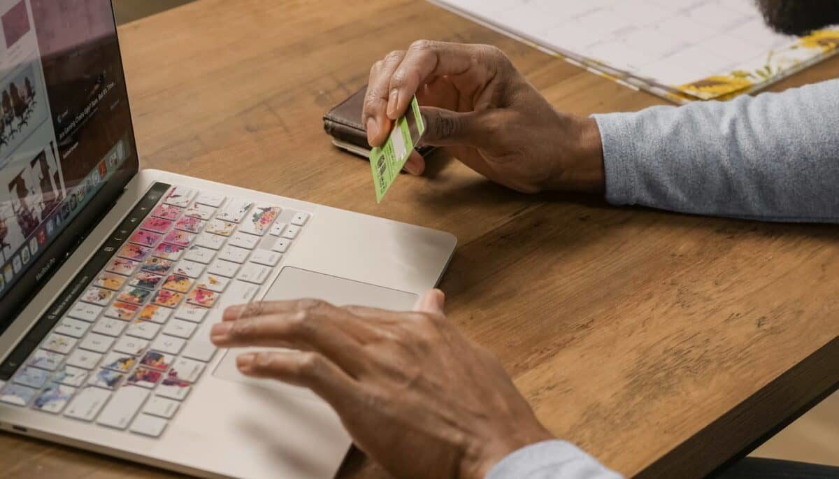 Imagem de uma pessoa mexendo no notebook com um cartão na mão, representando como vender parcelado.