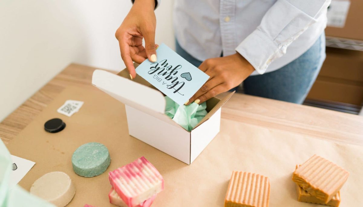Una mujer agrega a una caja una tarjeta de sus frases para agradecer la compra de un producto.