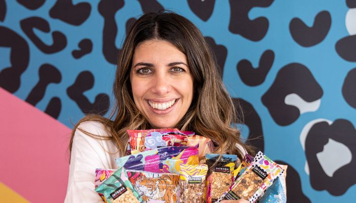 Mujer (Laura Romano) sostiene paquetes de ÍNTEGRA, su marca de alimentos saludables, naturales y ricos.