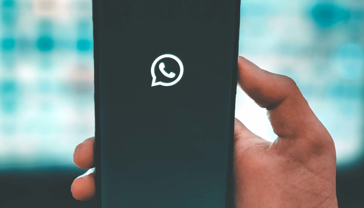 Mano sostiene celular con la pantalla de inicio de mensaje de bienvenida en whatsapp business ejemplos