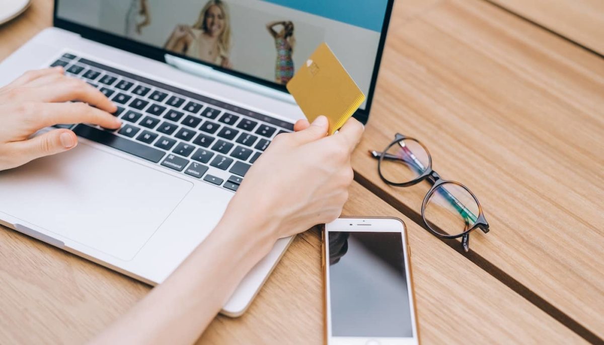 Pessoa fazendo compras online com um cartão de crédito na mão, representando o que é intermediador de pagamento.