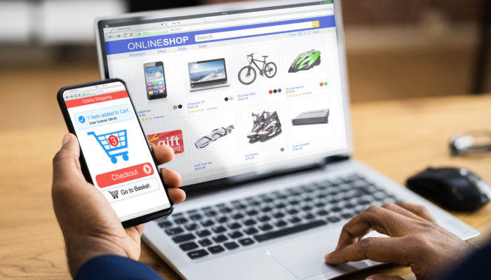 fotografía de una persona con un celular y una computadora portatil comparando que plataforma de comercio electronico elegir, si Jumpseller o Shopify