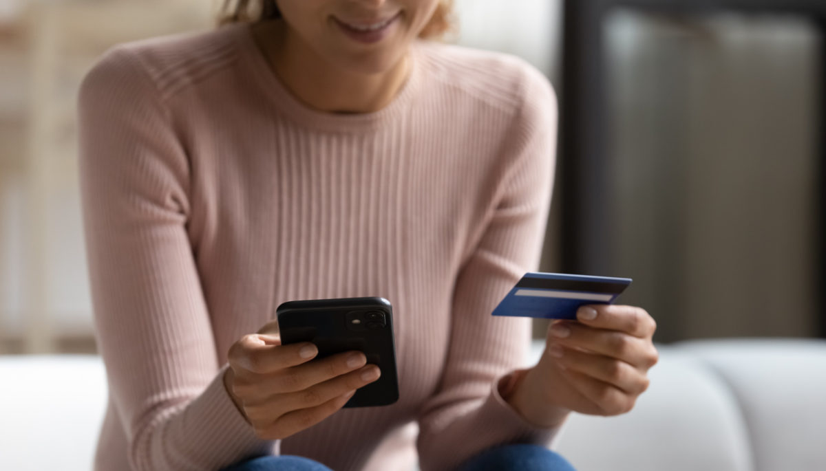 fotografia de una mujer utlizando su telefono y tarjeta de credito para hacer un cobro en linea