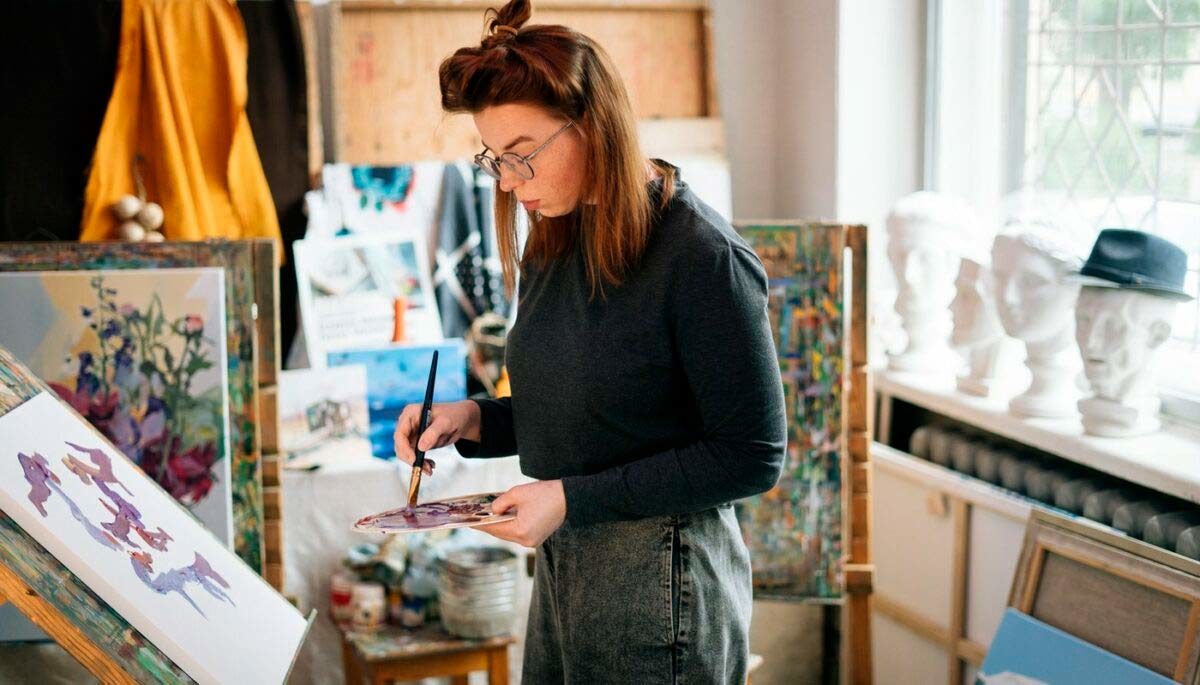 Imagem mostrando uma mulher fazendo uma pintura em tela, representando como fazer quadros decorativos para vender.