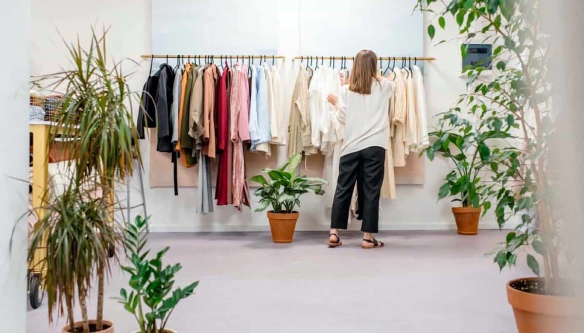 Imagem de uma mulher escolhendo roupas na arara de uma loja, representando como vender na AMARO.