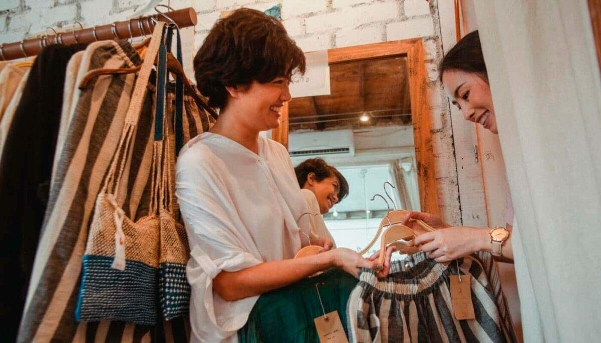 Mulher sorri enquanto interage com vendedora em loja de roupas, representando uma boa experiência do cliente
