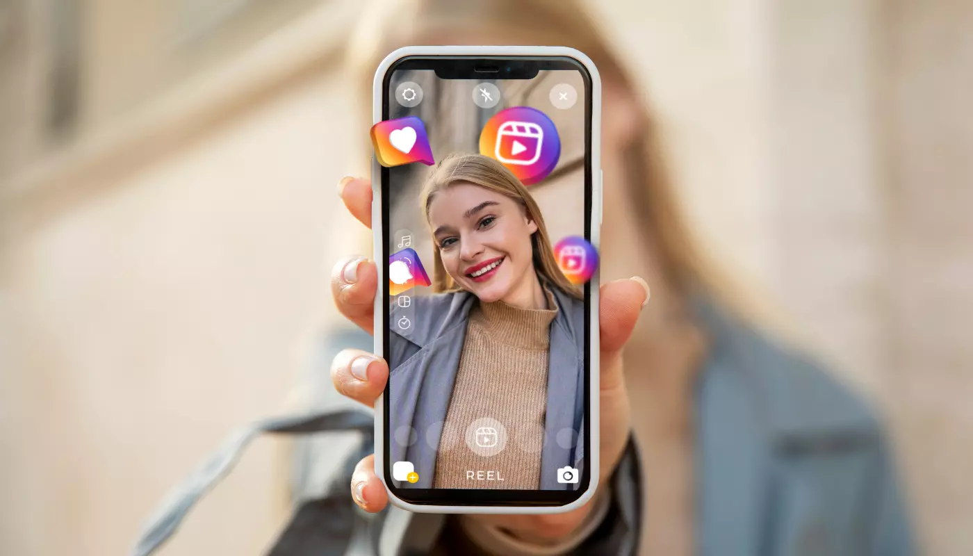 Mulher loira segura um telefone virado para o usuário. Na tela, vemos que era está usando o modo câmera no Instagram.
