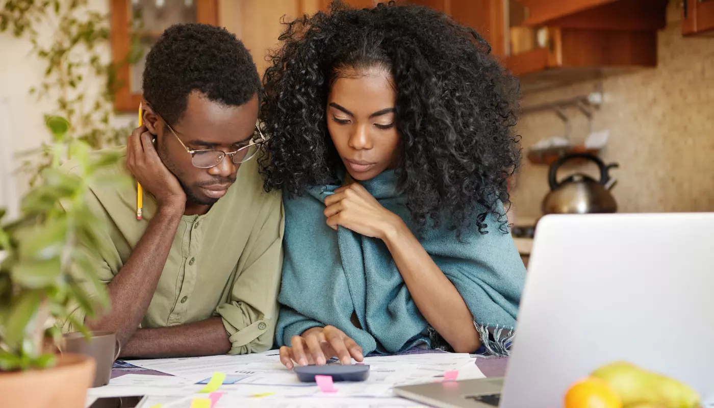 Casal de empreendedores negros está sentado a frente de uma mesa com vários papeis e calculadoras aprendendo o que é contabilidade.