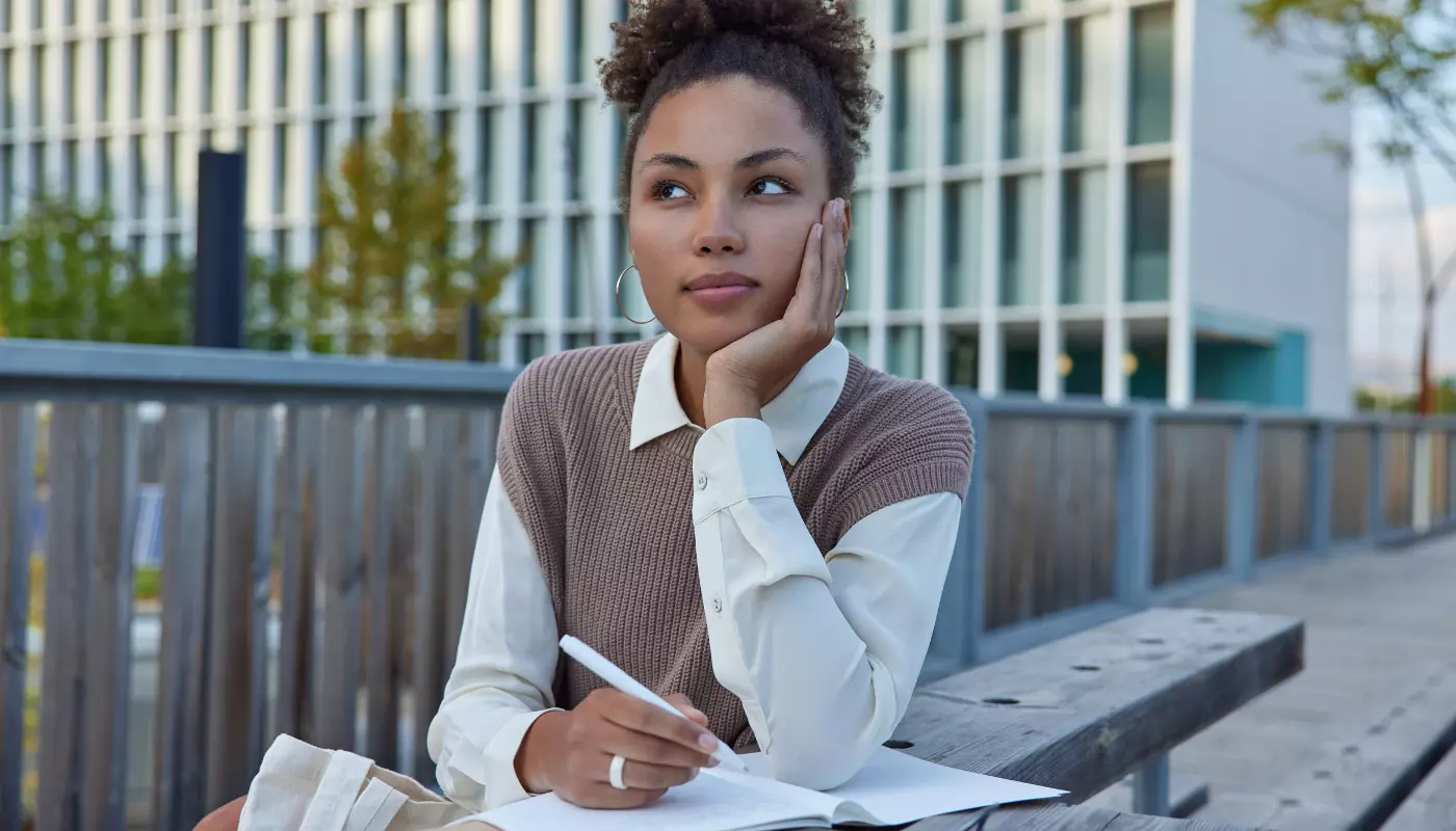Mulher está sentada de frente para um banco com um caderno aberto mostrando uma checklist.