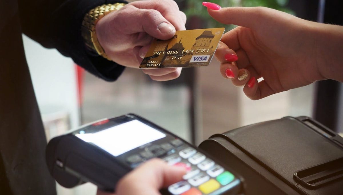imagem mostra mulher aceitando cartão de cliente, portando maquininha de cartão, para representar texto sobre split de pagamento
