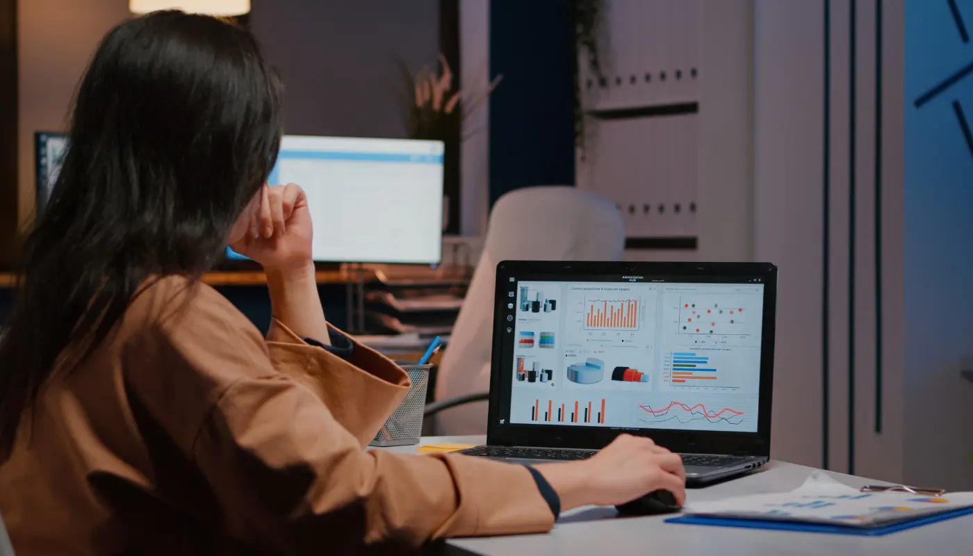 Mulher de costas mexendo no mouse de um notebook com a tela aberta mostrando gráficos dos funis de conversão do Google Analytics.