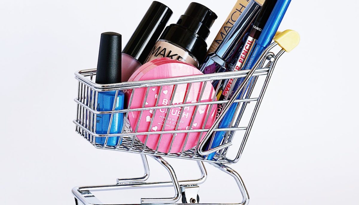 Na imagem, vemos um carrinho mini de supermercados com itens de maquiagem.