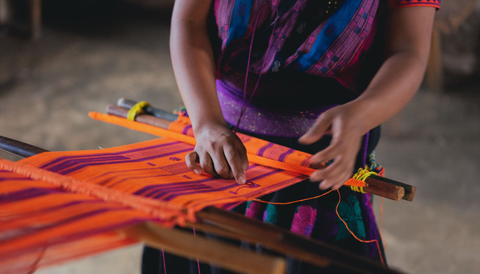 Mujer tejiendo con telar de cintura para vender por internet