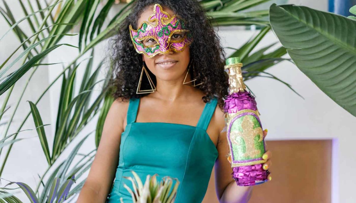 Empreendedora negra com máscara carnavalesca segura uma garrafa estilizada que pretende promover em uma campanha de carnaval.