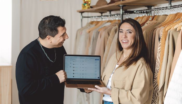 Dos emprendedores con canales de venta online y local físico sonríen mientras ven su tienda virtual en la notebook.