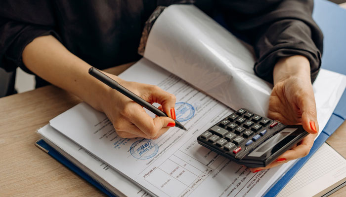 Una emprendedora evaluando su capital de trabajo en su carpeta con la ayuda de una calculadora.