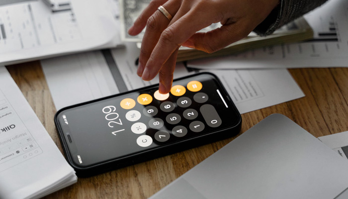 La mano de una emprendedora calculando su capital social con la ayuda de un smartphone.