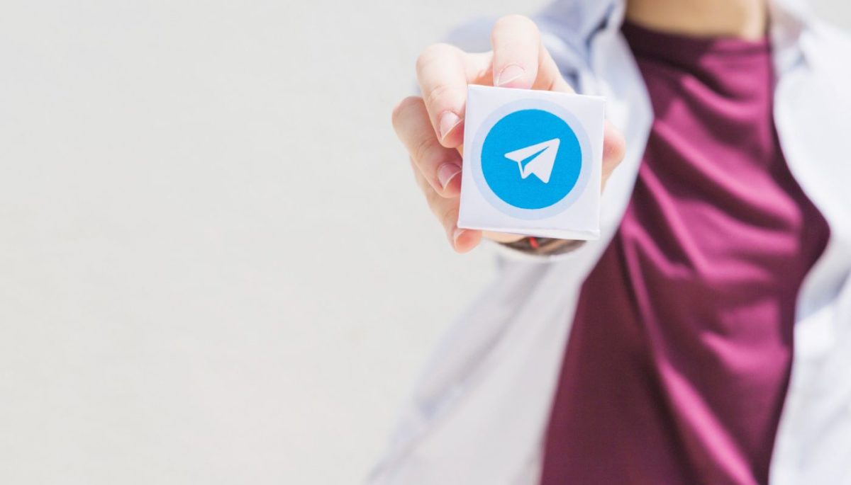 Homem segura bloco de notas com logo do telegram, ilustrando texto grupo de vendas do Telegram
