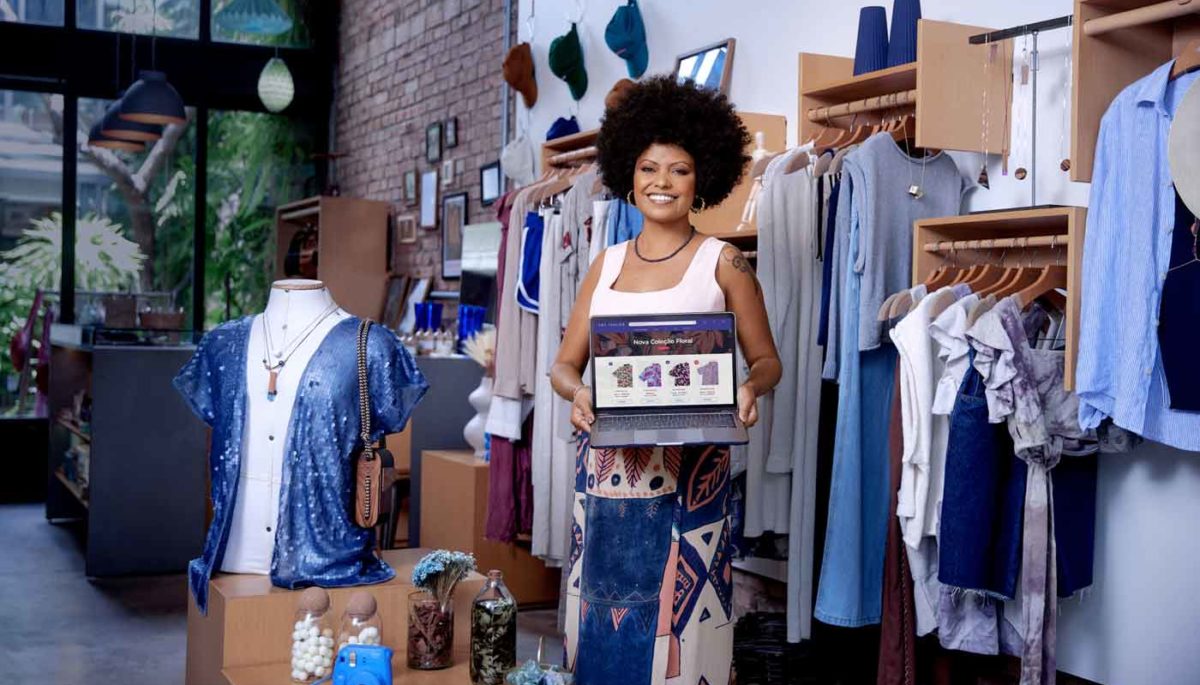Empreendedora negra posa em sua loja de roupas com um notebook mostrando sua loja virtual do mercado de moda.