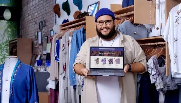 ¿Cómo crear una tienda online en Tiendanube para vender ropa? Diseñador de una marca de moda en su punto de venta físico mostrando en una laptop su tienda online de ropa creada con Tiendanube.