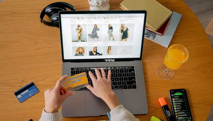 Qué es el checkout y cómo optimizarlo en tu tienda online El escritorio de una mujer que sostiene su tarjeta de crédito en la página de checkout de una tienda online de ropa.