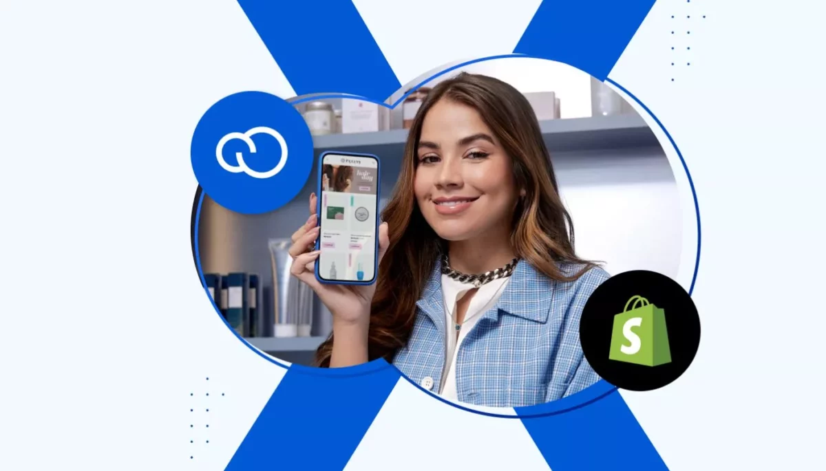 Jovem empreendedora posa exibindo sua loja virtual na tela do celular. Ao fundo, vemos o símbolo de um X e os logos da Nuvemshop e da Shopify, ilustrando o comparativo entre as plataformas.