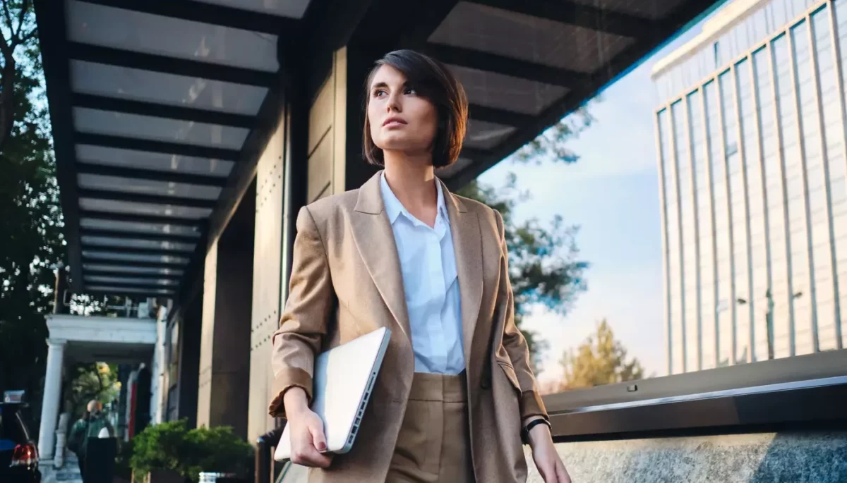 Mulher com roupas formais andando com um notebook em uma das mãos, representando profissões mais bem pagas do Brasil.