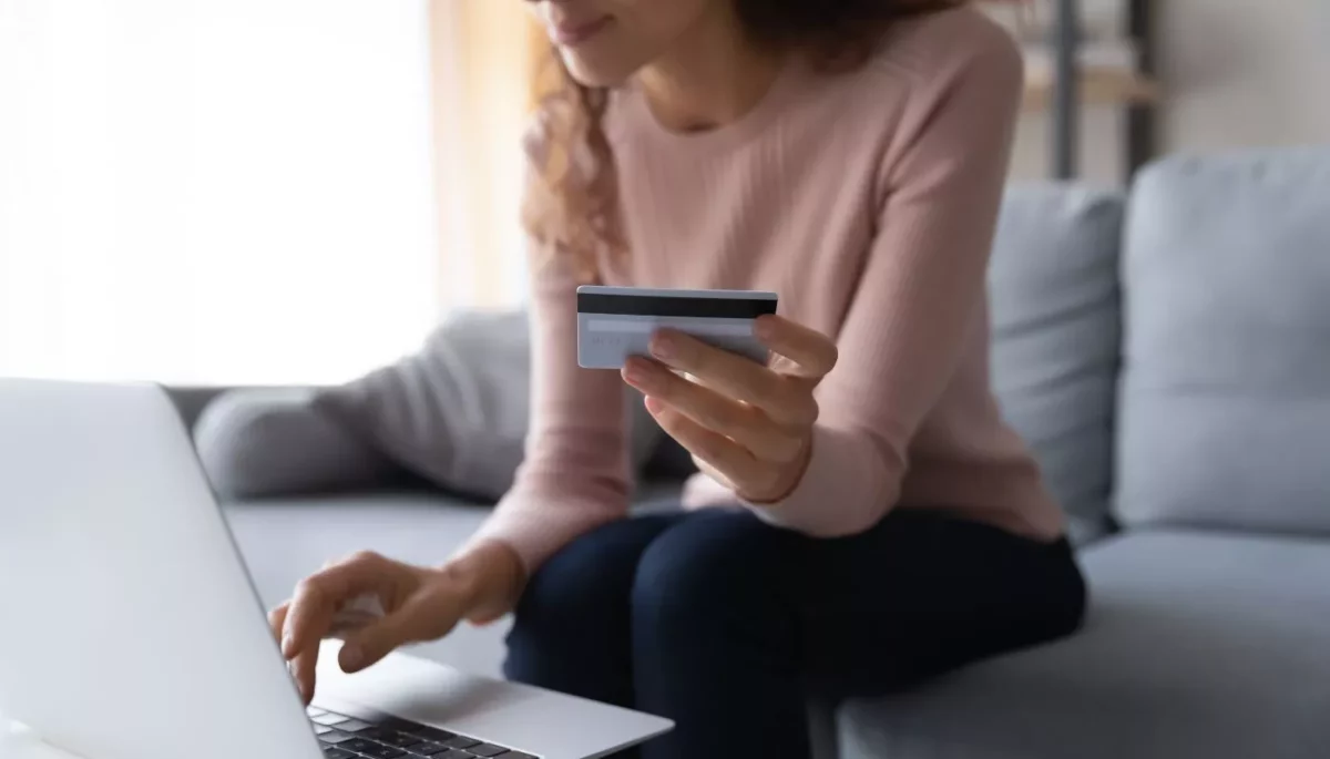 Código promocional: como escalar e vender mais em 2025 Imagem de mulher finalizando uma compra online no sofá de sua casa, usando um código promocional